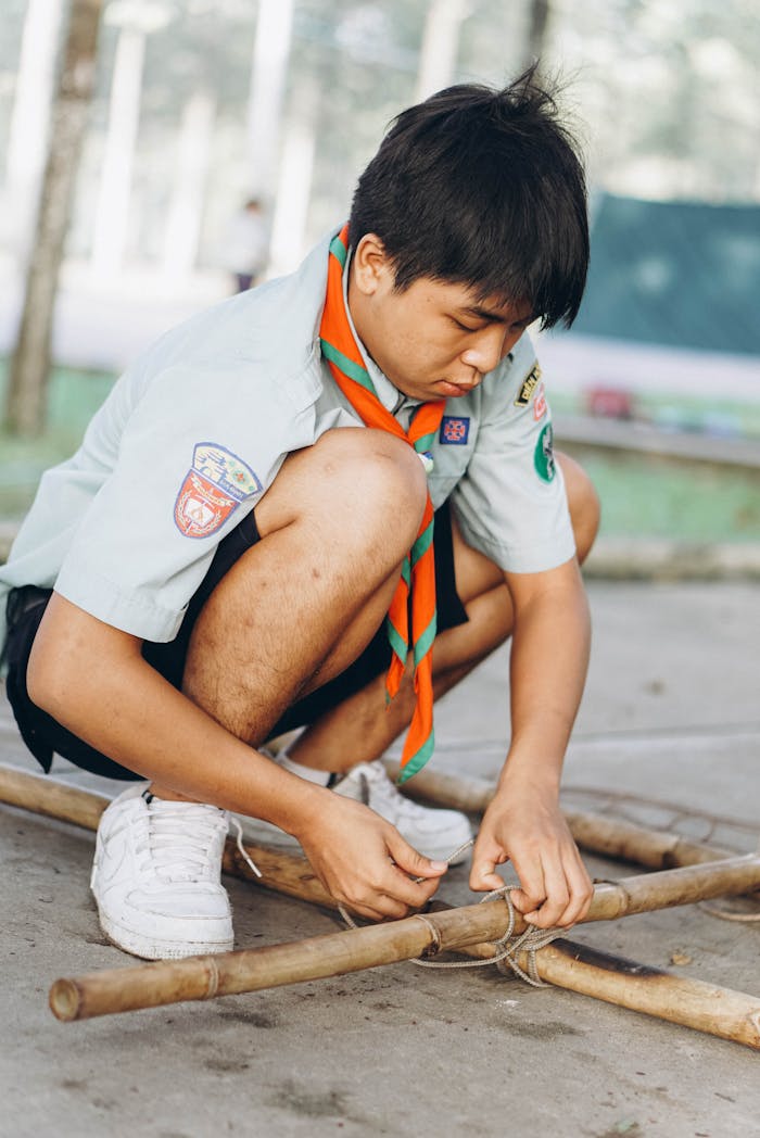 The Art of Drawing Readers In: Your attractive post title goes here A scout tying knots on bamboo sticks during an outdoor activity, showcasing teamwork and learning.